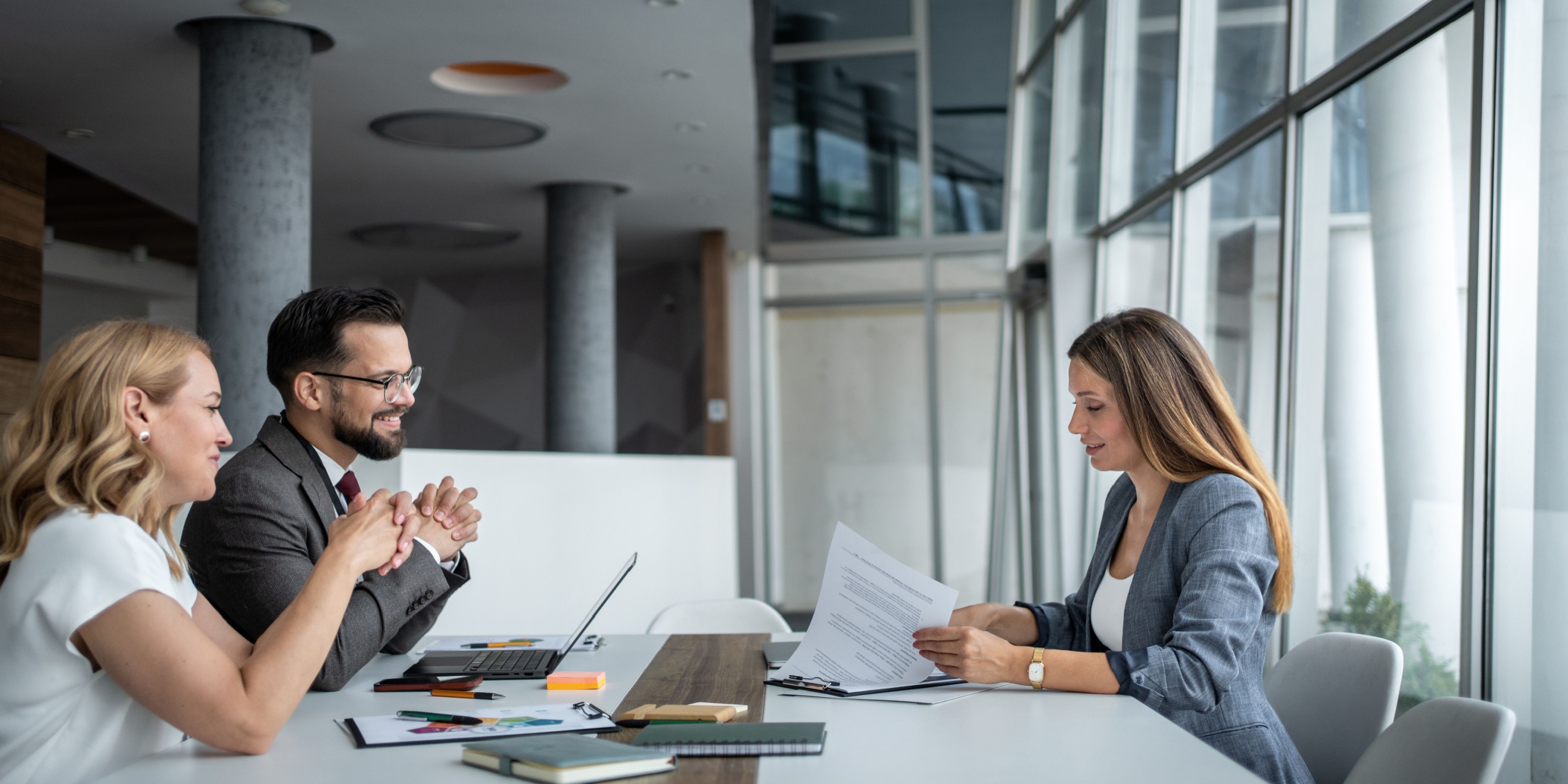Client Meetings in Coworking: How to Make a Great Impression Business partners sitting at desks in modern offices, listening as a female manager presents the contract’s terms and conditions during a business meeting.