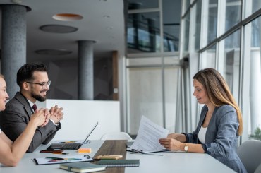 Business partners sitting at desks in modern offices, listening as a female manager presents the contract’s terms and conditions during a business meeting.