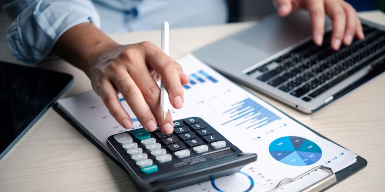 The Hidden Costs of Flex: Cancellation Policies, Minimums, Overages Finance analyst using a calculator while working on a budget report with charts on a laptop in the office, reviewing data, accounting, numbers, analysis, planning, costs, and profit for decision-making.