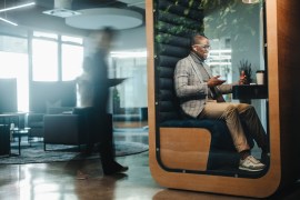 Businessman working in a busy privacy booth, having a video call on his laptop. The young entrepreneur is fully engaged in the virtual meeting, discussing business matters with a client.