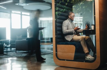 Businessman working in a busy privacy booth, having a video call on his laptop. The young entrepreneur is fully engaged in the virtual meeting, discussing business matters with a client.