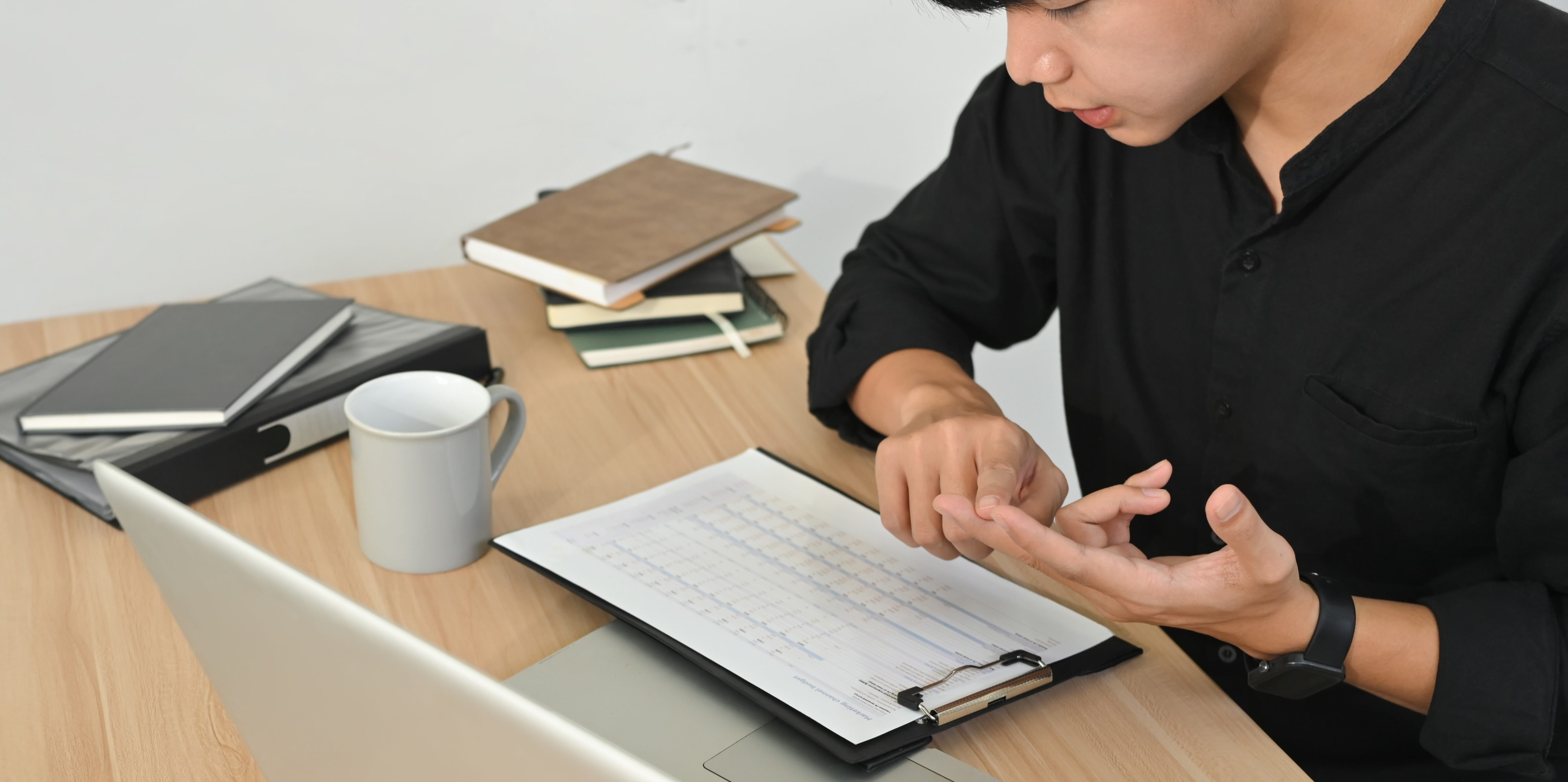 Economic Uncertainty and Office Spend: How Small Businesses Stay Flexible in 2026 Focused businessman reviewing charts and data on clipboard while working at desk with laptop