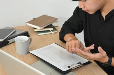 Focused businessman reviewing charts and data on clipboard while working at desk with laptop