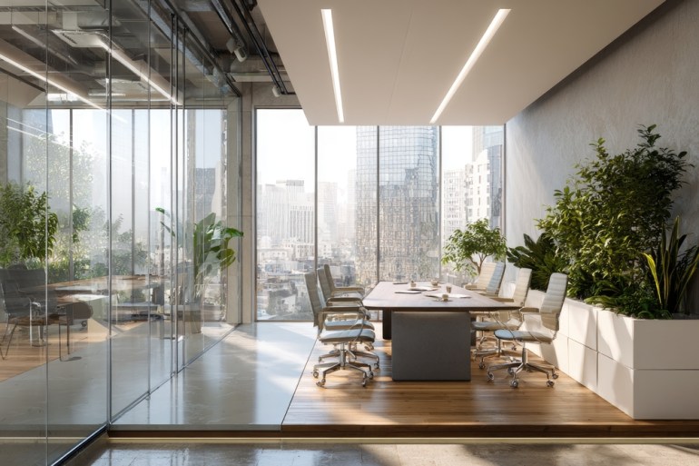 A modern, sunlit office conference room features a large window overlooking the city skyline. The room is elegantly furnished, with a long table, chairs