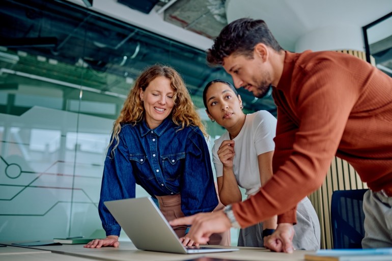 Diverse business teams collaborating and discussing project strategy, pointing at a laptop screen in a modern office