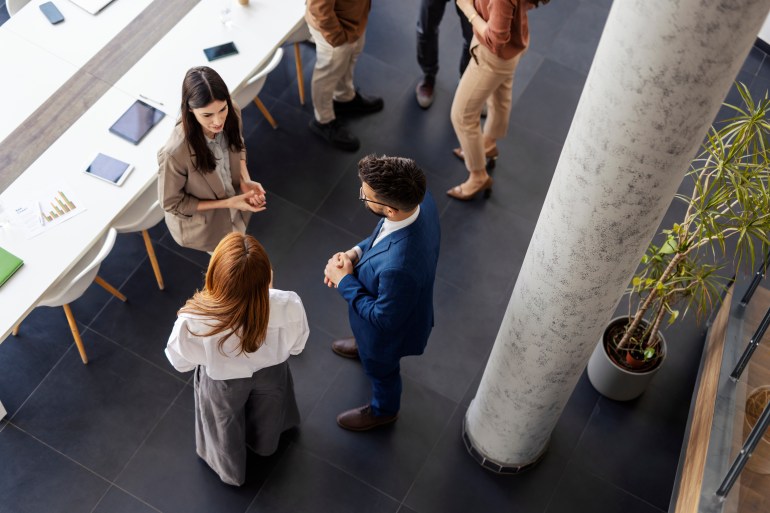 aerial view of three people, two women and a man, talking in an office setup 