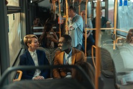 An image focusing on two people sitting in the bus, talking. They are smiling and surrounded by other people taking the bus.
